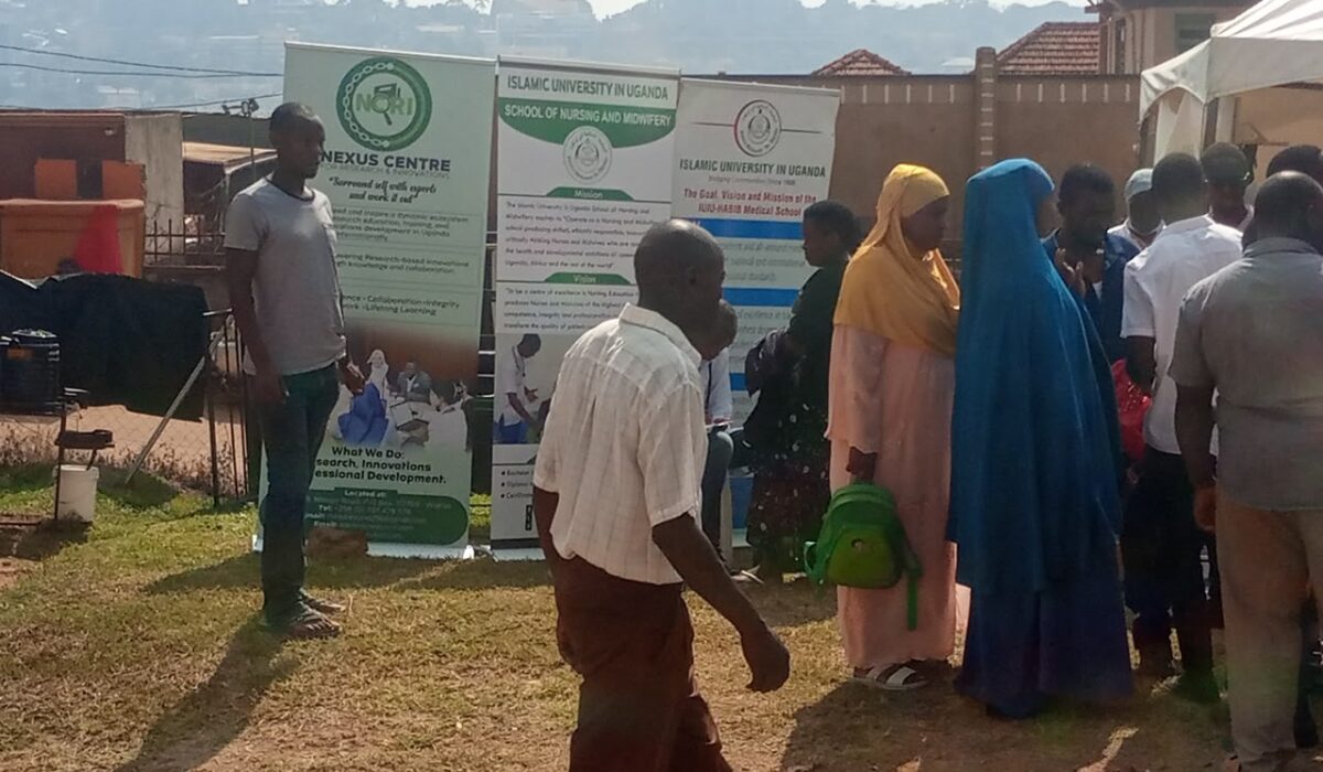 People gathered outdoors beside Nexus Centre and Islamic University in Uganda banners during an engagement activity.